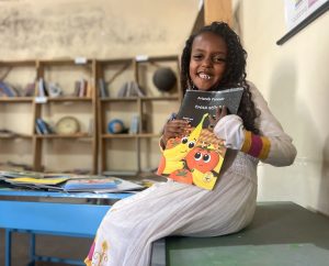 Smiling Ethopian girl holding "Friends Forever" by Ready Set Go Books