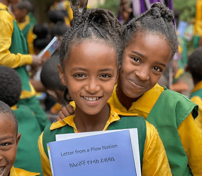 two-girls-holding-letters-from-a-plow-nation Two Ethiopian girls in green and yellow uniforms holding the Ready Set Go book "Letters from a Plow Nation"