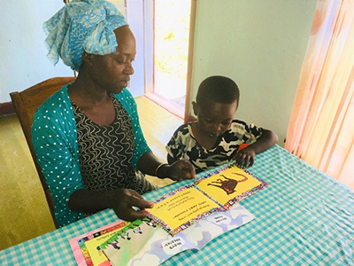 Ethiopian woman reading bilingual picture book with young boy at a table with a ginham table cloth